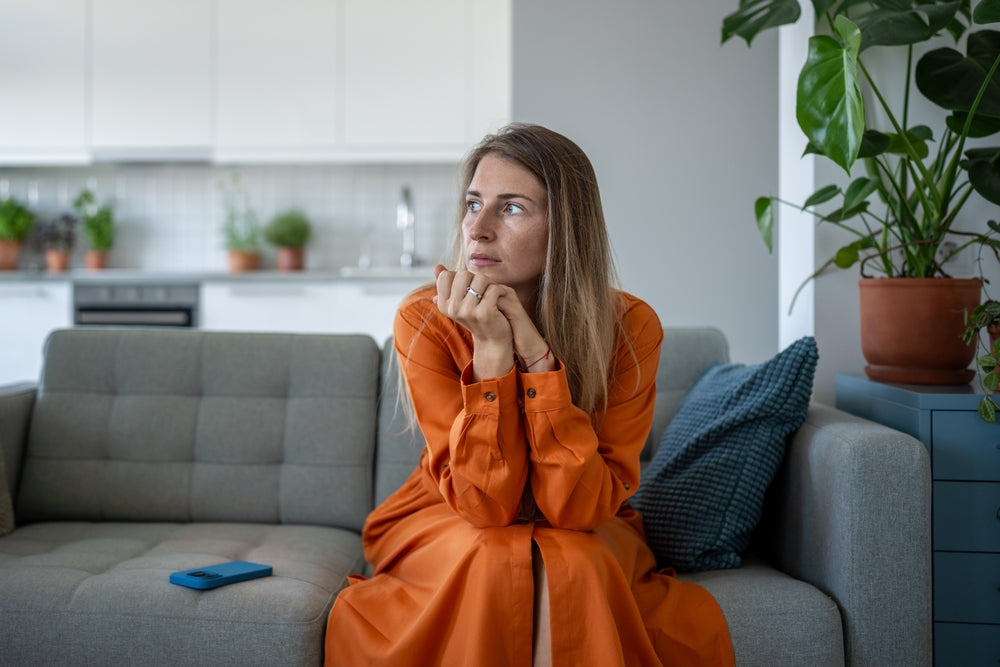 woman in orange dress sitting on a sofa looking concerned