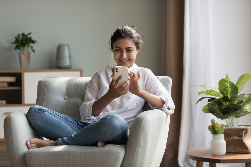 Woman sitting on a couch using a smartphone in a cozy living room.