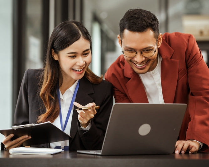 Two people working together on a laptop in an office setting