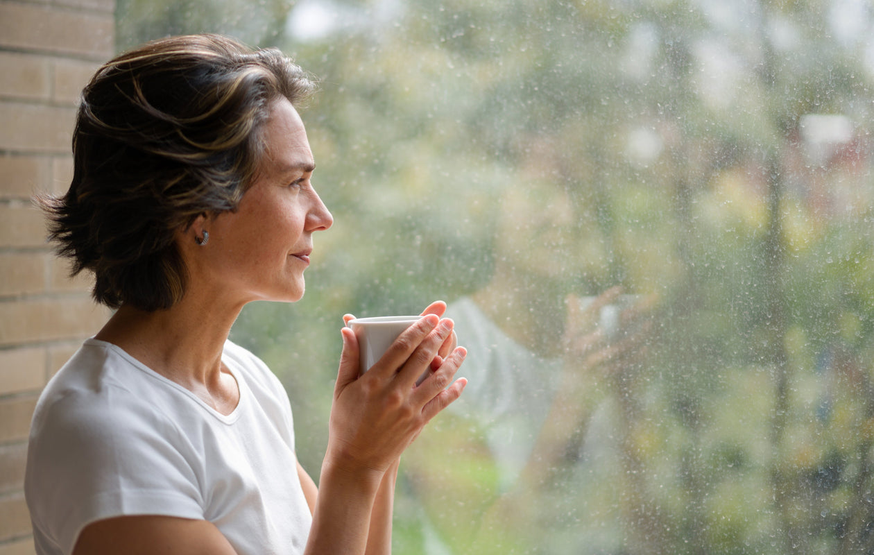 Woman holding a mug, looking out a window on a rainy day